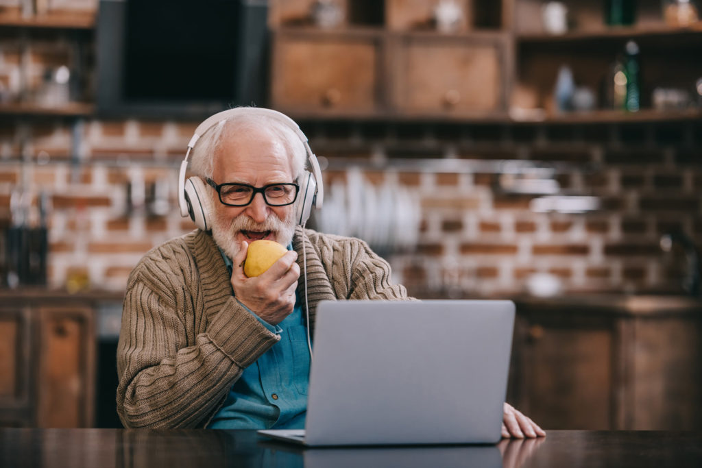 old man with headphones eatin fruit in front of his laptop
