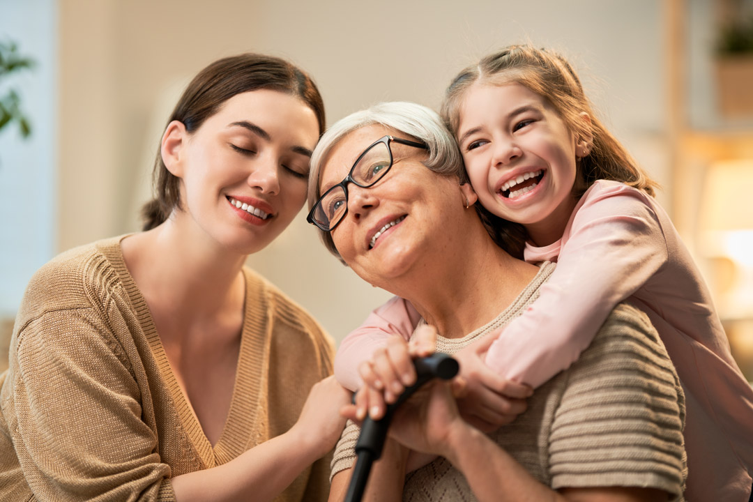 Grandma, her daughter, and her granddaughter are hugging together, while smiling.